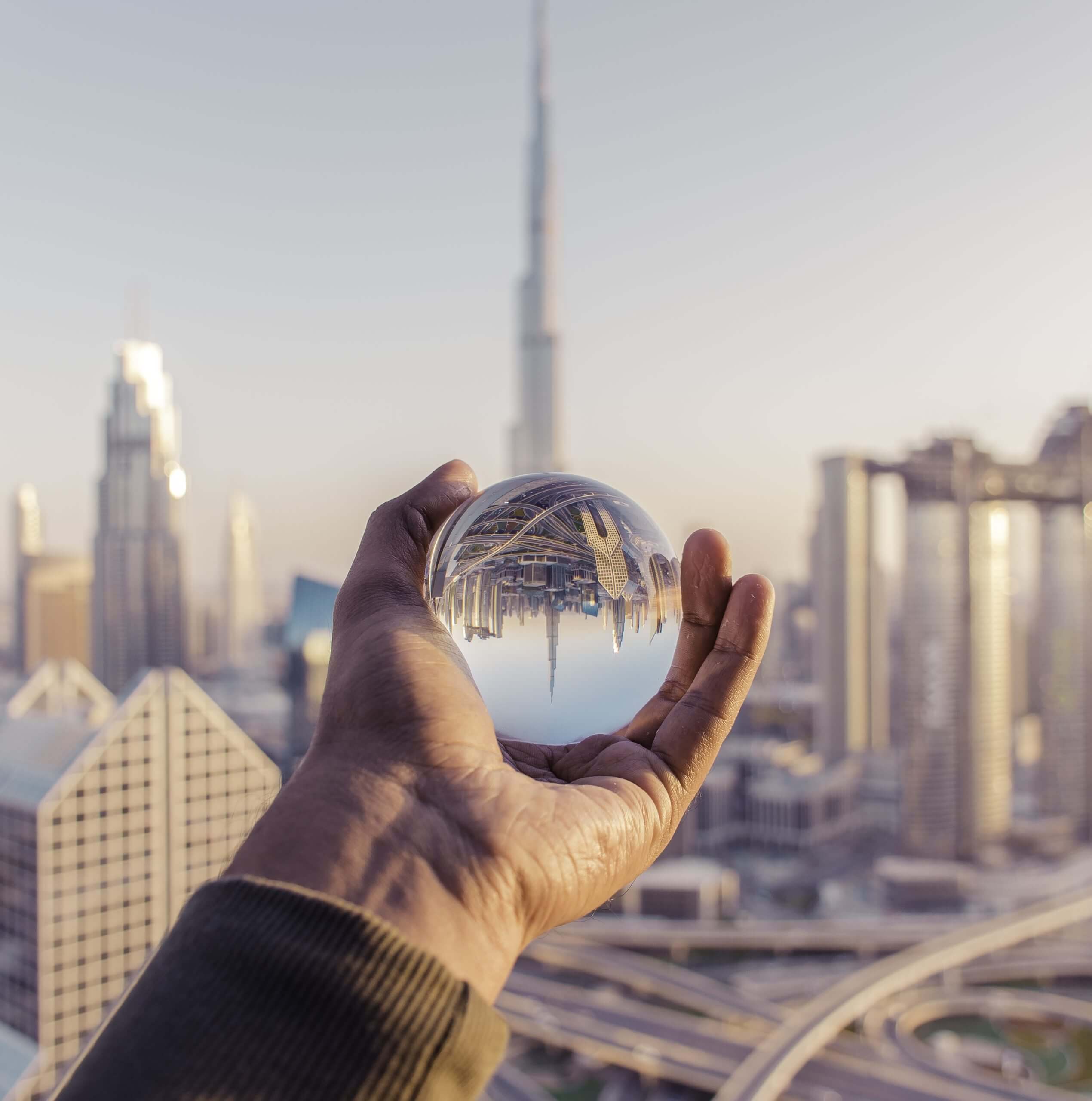 Male hand holding crystal ball reflecting Dubai's premier properties, showcasing PJ International, the city's top real estate agency.